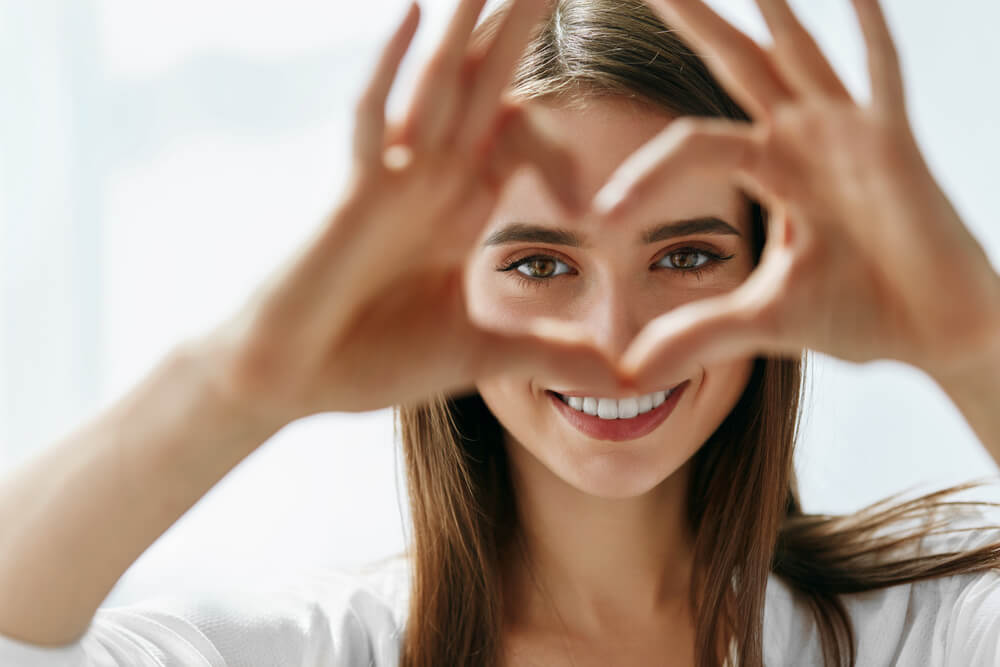 Young woman making a heart with her hands over her face